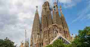 Sagrada Família basilica in Barcelona with tall ornate spires and blue sky, some construction cranes nearby
