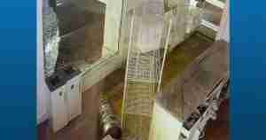 Store interior with a broken storefront window, toppled metal wire shelving, and scattered debris on the floor.